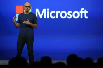 Satya Nadella sur scène lors d’une présentation Microsoft, devant un fond bleu avec le logo de l’entreprise