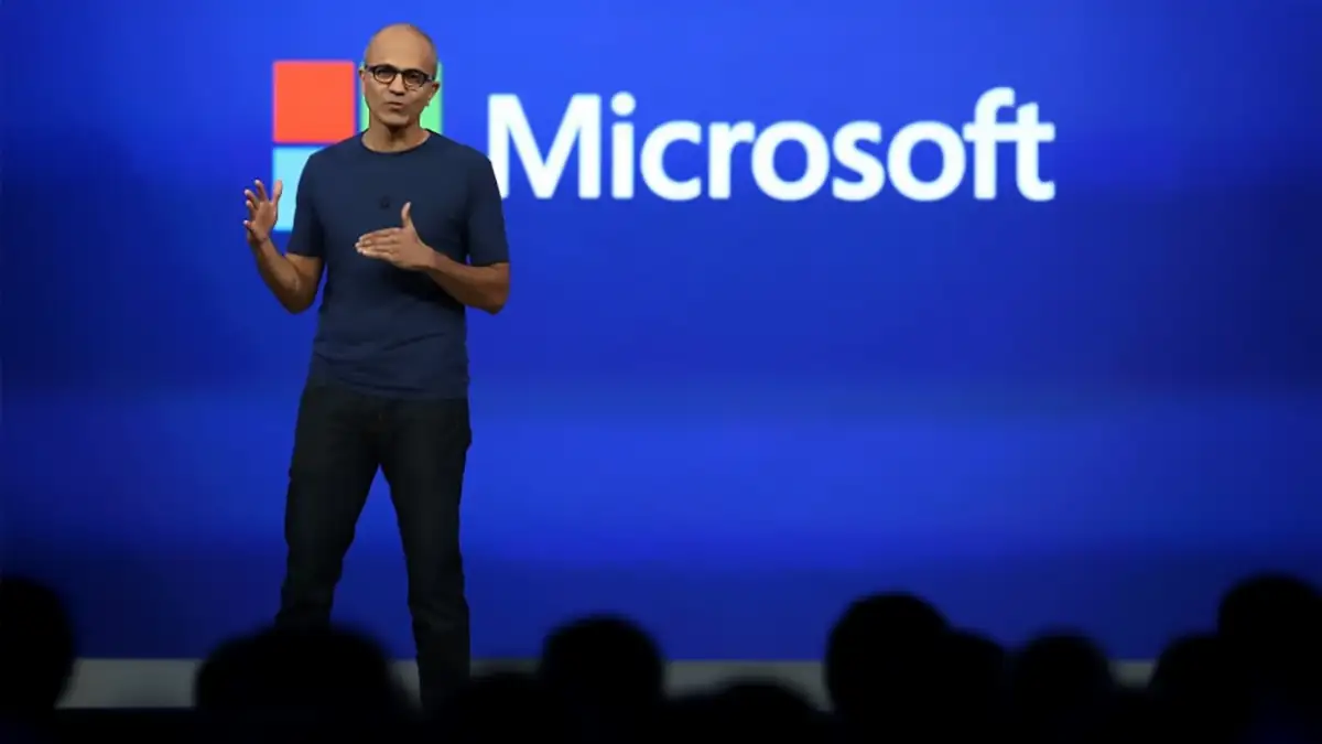 Satya Nadella sur scène lors d’une présentation Microsoft, devant un fond bleu avec le logo de l’entreprise