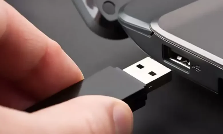 Une clé USB noire connectée à un port USB d'ordinateur portable, illustrant l'action de brancher un périphérique de stockage.