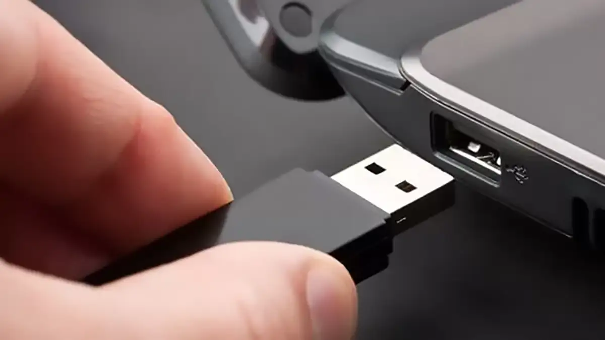 Une clé USB noire connectée à un port USB d'ordinateur portable, illustrant l'action de brancher un périphérique de stockage.