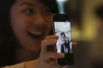 Une femme souriante montre l'écran d'un smartphone affichant une photo d'elle en train de saluer.