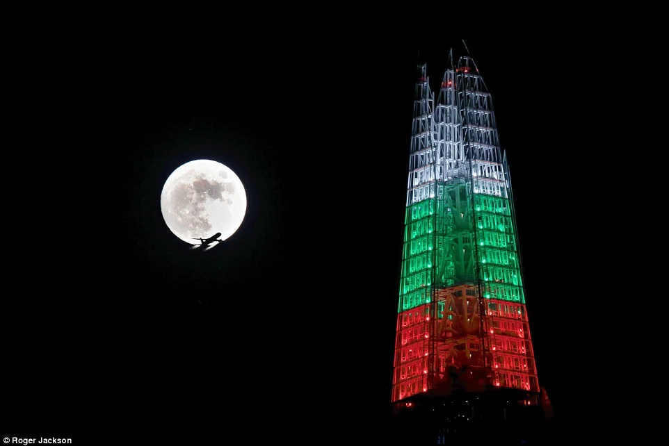 Un avion vole devant la pleine Lune froide qui illumine le ciel de Londres le soir de Noël. Même la tour Shard fait pâle figure à côté.