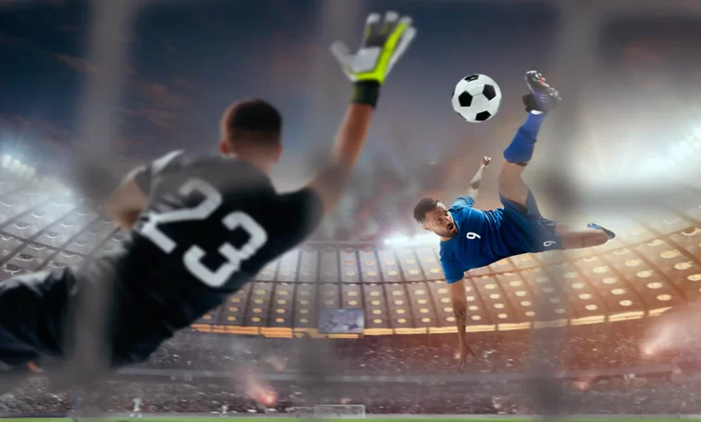 Un joueur de football en bleu effectue un retourné acrobatique face à un gardien tentant d'arrêter le ballon dans un grand stade illuminé.