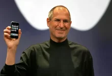 Steve Jobs tenant le premier iPhone lors de sa présentation officielle, vêtu de son col roulé noir iconique.