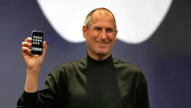 Steve Jobs tenant le premier iPhone lors de sa présentation officielle, vêtu de son col roulé noir iconique.