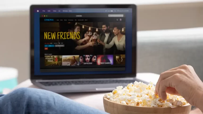 Personne mangeant du popcorn devant un ordinateur portable affichant un film en streaming. Plateforme de streaming légal pour regarder des films en ligne.