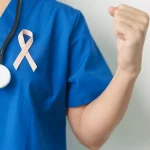 Un professionnel de la santé en blouse bleue tient un ruban rose, symbole de la lutte contre le cancer, avec un stéthoscope autour du cou.