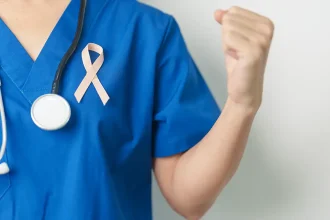 Un professionnel de la santé en blouse bleue tient un ruban rose, symbole de la lutte contre le cancer, avec un stéthoscope autour du cou.