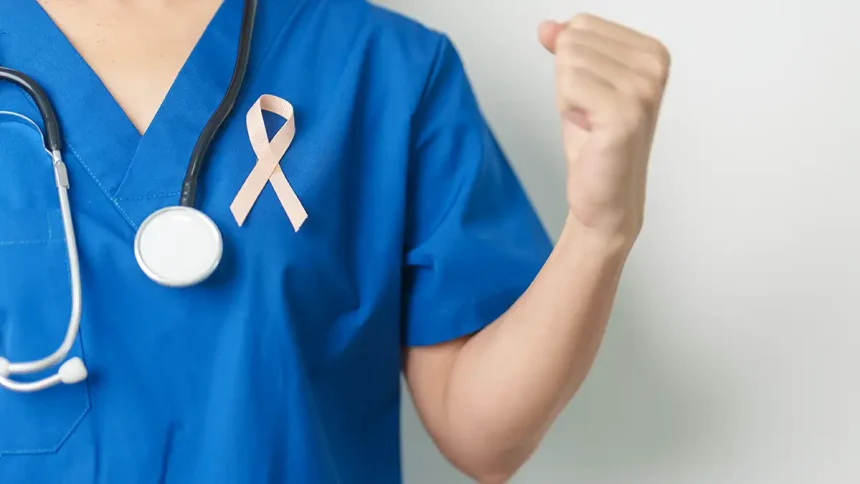 Un professionnel de la santé en blouse bleue tient un ruban rose, symbole de la lutte contre le cancer, avec un stéthoscope autour du cou.