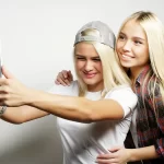 Deux adolescentes souriantes prenant un selfie avec une tablette, illustrant l'impact des réseaux sociaux sur les jeunes.