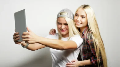 Deux adolescentes souriantes prenant un selfie avec une tablette, illustrant l'impact des réseaux sociaux sur les jeunes.