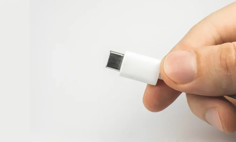 Un homme tenant un câble USB-C blanc, illustrant le concept d'un chargeur universel standardisé.