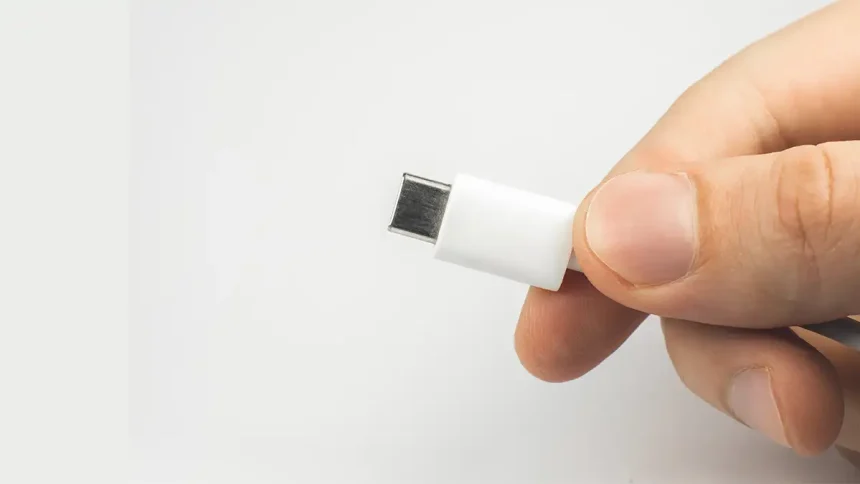 Un homme tenant un câble USB-C blanc, illustrant le concept d'un chargeur universel standardisé.