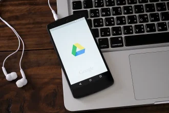 Logo de l'application Google Drive affiché sur l'écran d'un smartphone Android, posé sur le clavier d'un ordinateur portable. Illustration de l'accessibilité et de la synchronisation des données via le service de stockage cloud.