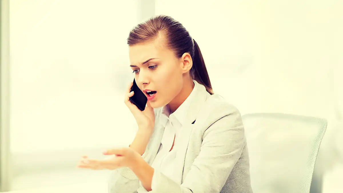 Femme stressée par appel téléphonique spam : expression de frustration et d'exaspération.