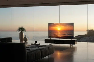 Téléviseur OLED LG installé sur un meuble bas devant une baie vitrée avec vue sur la mer au coucher du soleil.